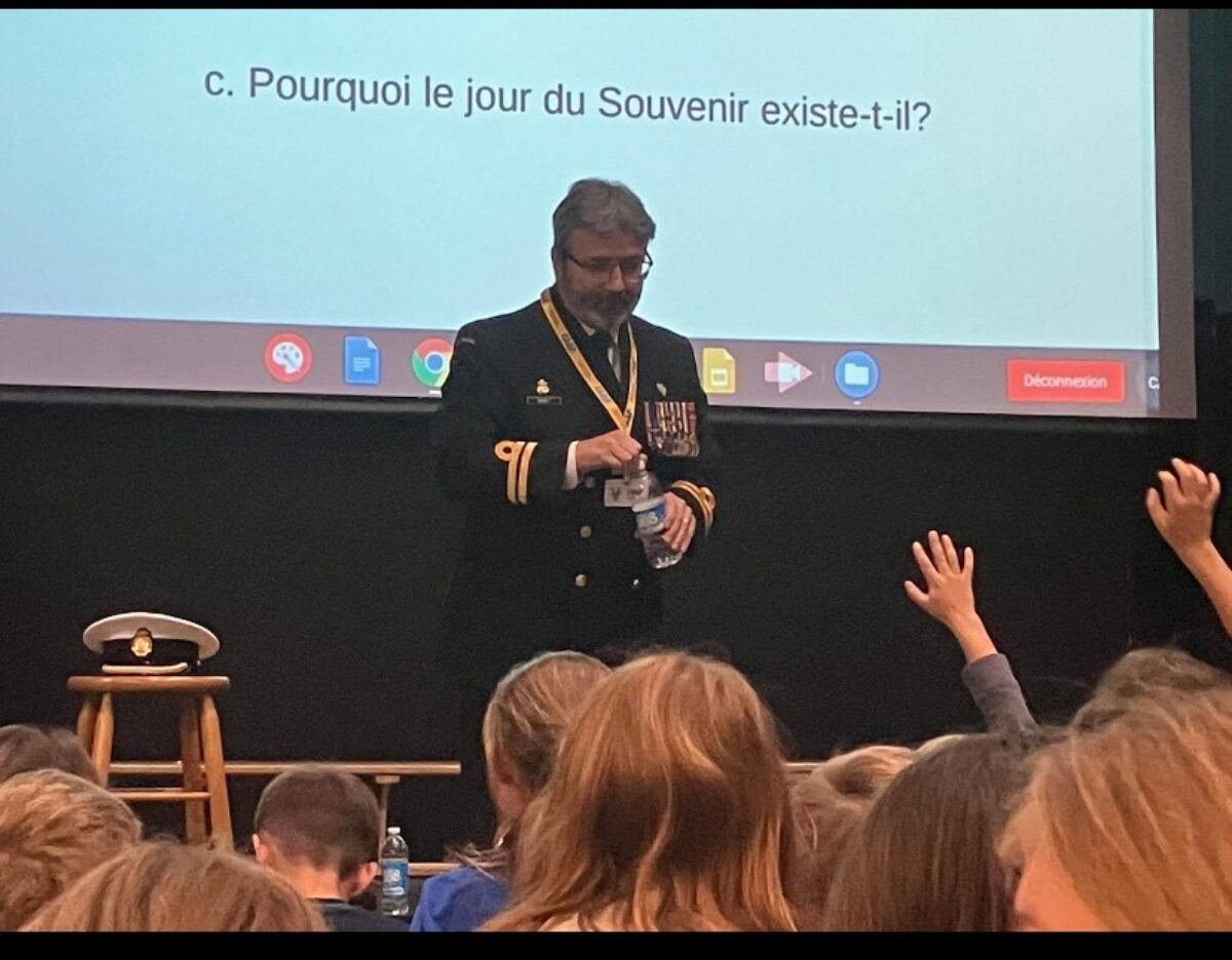 Un officier en uniforme devant un écran s'adresse à un auditoire d'étudiants.