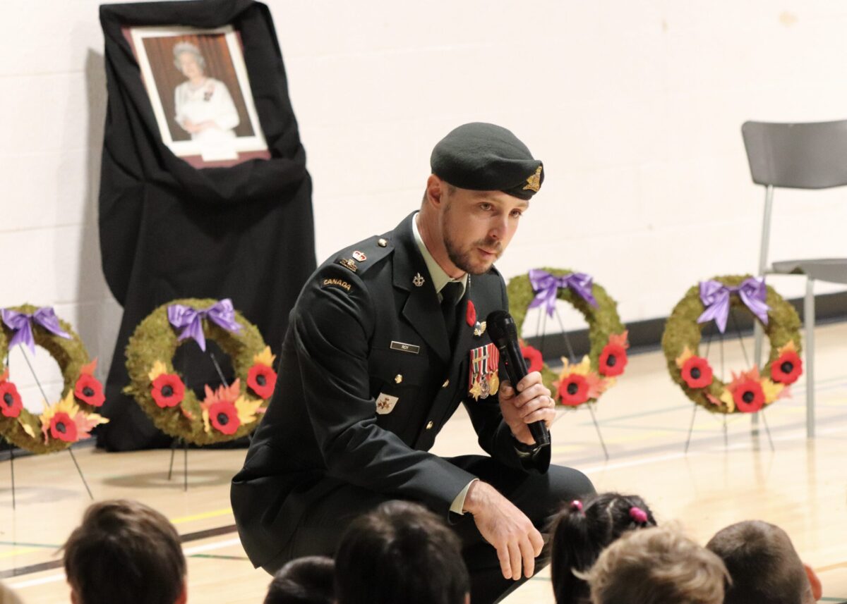 Un officier militaire en uniforme parle dans un microphone tout en s'adressant à un gymnase d'enfants.